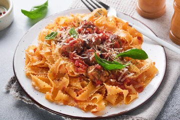 Tagliatelle pasta with meatballs in tomato sauce and thyme in sauce on light grey slate, stone or concrete background. Traditional Italian dish and cuisine. Top view with copy space.