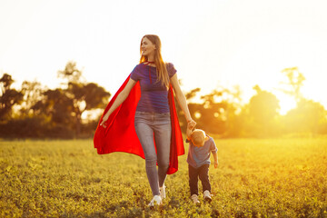 Super mom and her son are running forward. Cheerful family, woman in a red cape as a superhero