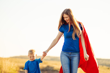 Super mom and her son walk forward holding hands. Cheerful family, a woman in a red raincoat as a...
