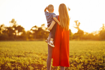 Happy loving family. Mom and her son are playing outdoors. Mom and her child in Superhero costumes....