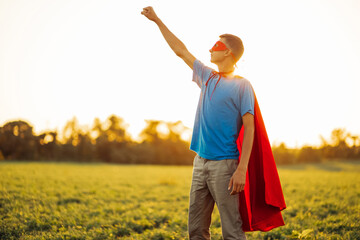 Joyful courageous man in a superhero costume poses on the field against the backdrop of sunset