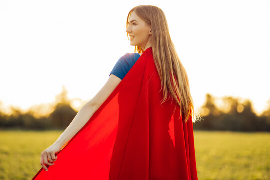 Woman superhero. A beautiful blonde in the image of a superheroine in a red cloak is growing up