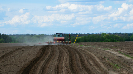 red tractor in a field rear view, tractor planting crops on an agricultural field. big red tractor working in the field, harvesting, business, agriculture. soil preparation, spring season. Ukraine