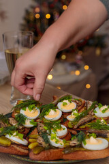 A woman's hand sprinkles a sandwich with sprats and an egg with herbs. Russian New Year food