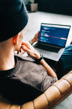 Young man mobile developer writes program code on a computer, programmer work in home office.