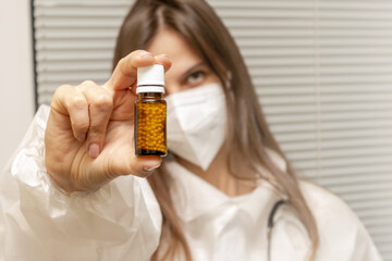 A young doctor wearing a mask holds a glass packet of medicine. A homeopathic medicine. Homeopathic treatment.