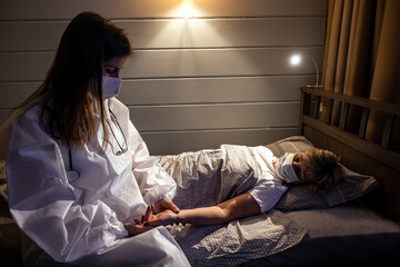 A young doctor in a protective mask sits on the bed next to the patient. A doctor visits the...