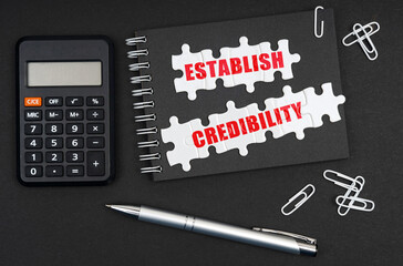 On the table is a calculator, a pen and a notebook with the inscription - Establish Credibility