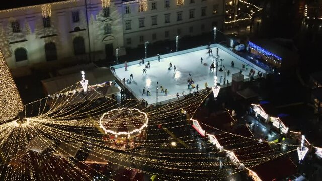Aerial drone view of The Big Square in Sibiu at night, Romania. Old city centre decorated for Christmas. Skating rink, old traditional buildings, people