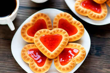 Fototapeta na wymiar Heart shaped red jam cookies and two cups of coffee on a brown wooden background.