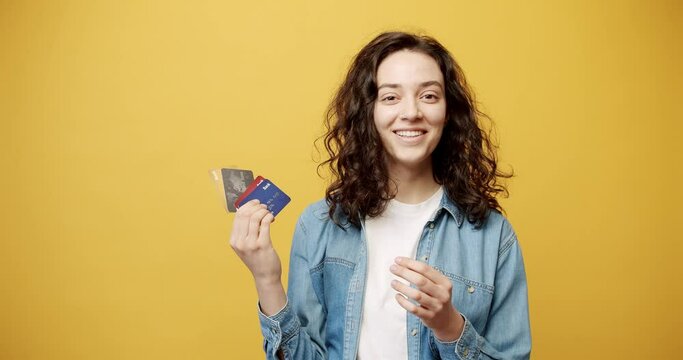 Happy smiling girl posing with a credit card in her hand, filmed in the studio. Smiling 20-year-old girl posing isolated on yellow background studio. The concept of people's lifestyle. 