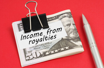 On a red background lies a pen and dollars clamped with a clip with the inscription on paper - Income from royalties