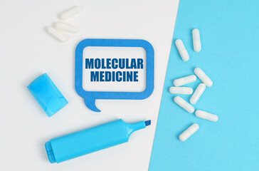 On a white and blue table are pills, a marker and a blue plaque with the inscription - Molecular Medicine