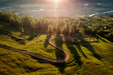 Beautiful curvy country road with fir trees in background during the sunrise with rays of light. Comanesti, Romania.
