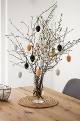 Fresh flowering branches decorated with easter colorful eggs in a vase on a wooden table.