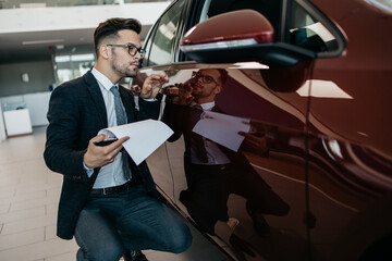 Car seller working in showroom and quality control checking of car details for the last time before...