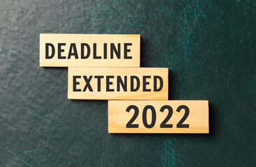 There is a blue notebook on a light gray background. Above are three wooden blocks with the words dEADLINE EXTENDED