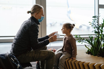 Obraz premium Father putting face mask on Childs face at the airport. Man protects girl from coronavirus at public place. Safe family travel concept. 