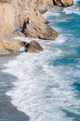Aerial top view of sea waves hitting rocks on the beach with turquoise sea water. 