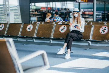 Girl wearing protective face mask with backpack in international airport at check-in counter, giving her passport to an officer and waiting for her boarding pass. Traveling during pandemic.
