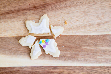 A single broken sugar cookie on a wooden cutting board; Pieces of one homemade sugar cookie