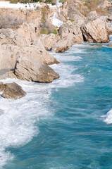 Aerial top view of sea waves hitting rocks on the beach with turquoise sea water. 