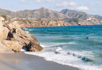 Aerial top view of sea waves hitting rocks on the beach with turquoise sea water. 