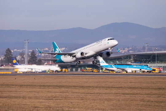 Air Dolomiti airplane departing aerodrome Graz for a flight to Munich with airport buildings and other airplanes on the apron in the background 