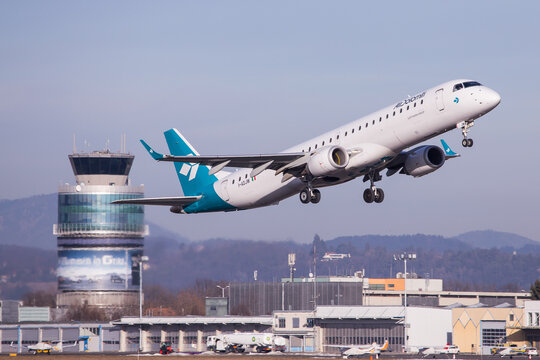 Air Dolomiti airplane departing aerodrome Graz for a flight to Munich with airport buildings and air traffic control tower in the background