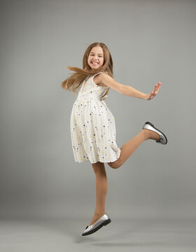 the concept of happiness, freedom, power, movement and people - a smiling young girl jumps in the air on a gray background