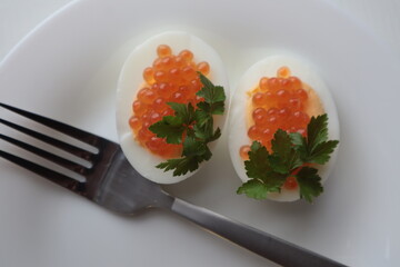 Red caviar with parsley lies on boiled and chopped eggs on a plate, top view.