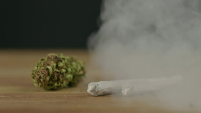Dried marijuana pothead and two rolled weed joints in a smoke cloud, on the black background, handheld close-up shot. Illegal marijuana use and street drug business concept with police lights.