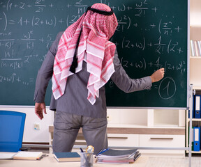 The arab teacher wearing suit in front of chalkboard