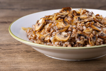 Fototapeta na wymiar Buckwheat porridge with mushrooms in a white plate on wooden background