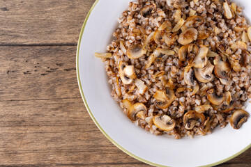 Buckwheat porridge with mushrooms in a white plate on wooden background