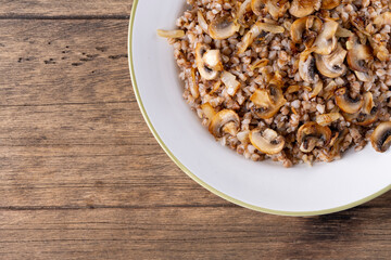 Buckwheat porridge with mushrooms in a white plate on wooden background