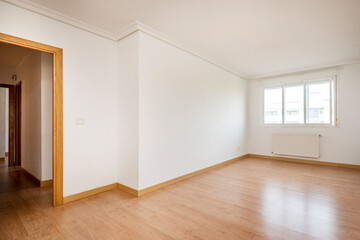 Large empty living room with light oak hardwood floors, bay window on one wall and white aluminum radiator