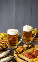 Mugs of cold beer with foam served on a wooden table with salty snacks in a wooden bowl
