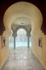 Arched corridor that leads to a room with a swimming pool and twin arches