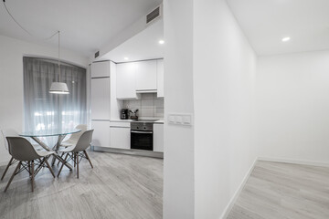 Hallway and white kitchen with circular glass dining table and gray parquet floors