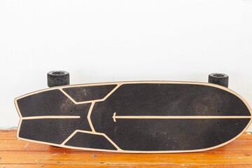 A black skateboard is placed on a white cement wall.