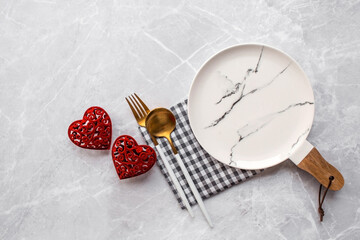 Banner. Table setting. A fashionable marble plate with a napkin, fork and red hearts on a gray background. Valentine's Day holiday concept for cafes and restaurants. A copy of the place for the text.