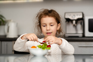 Two cute sisters' girls cut a salad from fresh vegetables. The girls are in the kitchen at home. They socialize and have fun while cooking. The concept of healthy eating. Healthy food. Childhood.