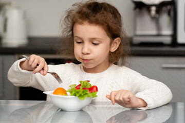 Two cute sisters' girls cut a salad from fresh vegetables. The girls are in the kitchen at home. They socialize and have fun while cooking. The concept of healthy eating. Healthy food. Childhood.