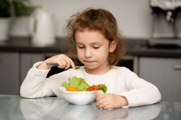 Two cute sisters' girls cut a salad from fresh vegetables. The girls are in the kitchen at home. They socialize and have fun while cooking. The concept of healthy eating. Healthy food. Childhood.
