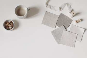 Artistic craft still life. Beige fabric linen swatches and silk ribbon isolated on white table background. Cup of coffee, bowl with walnuts. Neutral mood board project flat lay, top. Fabric samples.