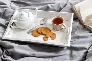 interior and home coziness concept. Top view. A cup of tea, a teapot with herbal tea, sugar bowl on a wooden tray on the bed. Porcelain cup