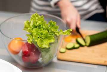 Fresh vegetables in a transparent plate on the table. Healthy eating. Nearby you can see the hands of a man who cuts a salad. The concept of healthy food. Health care.