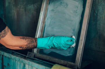 Male worker cleaning screen frame with a cloth in a printing workshop