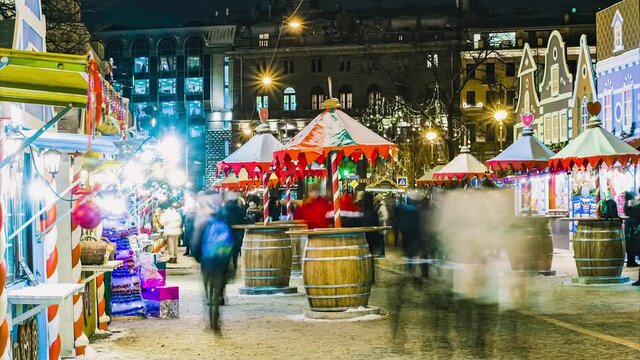 Timelapse of a Christmas street fair in the evening in the city center, people walk, buy gifts in tents, drink hot mulled wine